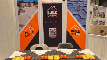Build Ops HQ tradeshow booth with branded banners, brochures, pens, and orange stress balls neatly arranged on a black tablecloth, set up in an exhibition hall.