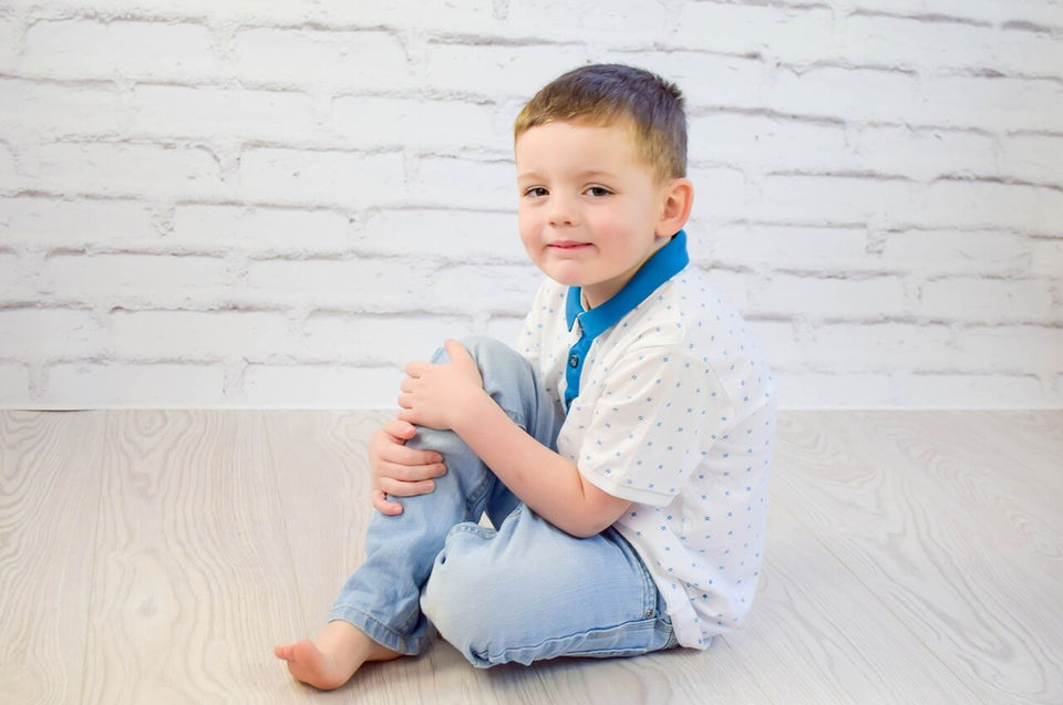 Ein 5-Jähriger Bub in weißem, gepunktetem Hemd und blauem Jeans wurde im Kindergarten fotografiert.