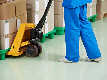 Worker in blue uniform using pallet jack to move cardboard boxes.