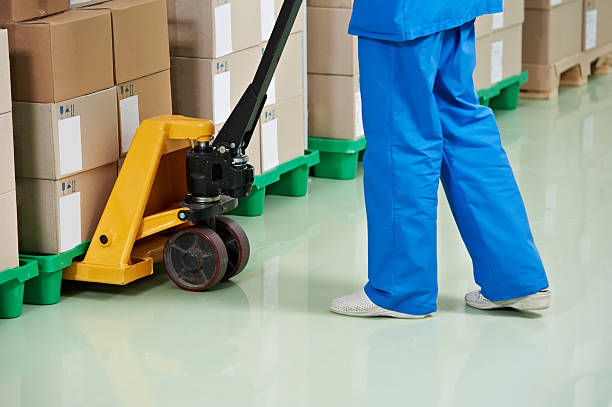 Worker in blue uniform using pallet jack to move cardboard boxes.