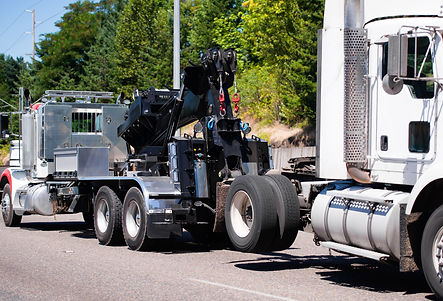 A powerful big rig semi truck tractor tows a broken white semi truck on a highway with gre