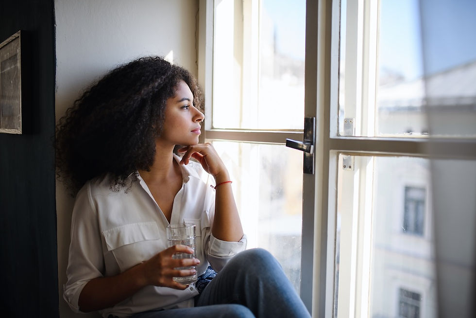 Nachdenkliche junge Frau sitzt mit einem Glas Wasser am Fenster