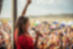 Woman in a red shirt sings into a microphone with one arm raised, facing a cheering crowd at Red Ants Pants Music Festival
