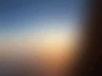 Sunset view from an airplane window, with a vibrant orange sun casting light over clouds and a clear blue sky, creating a serene mood.