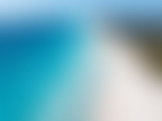 Aerial view of a pristine beach with turquoise waves, a lone kite surfer, and resort buildings in lush greenery. Bright, serene ambiance.