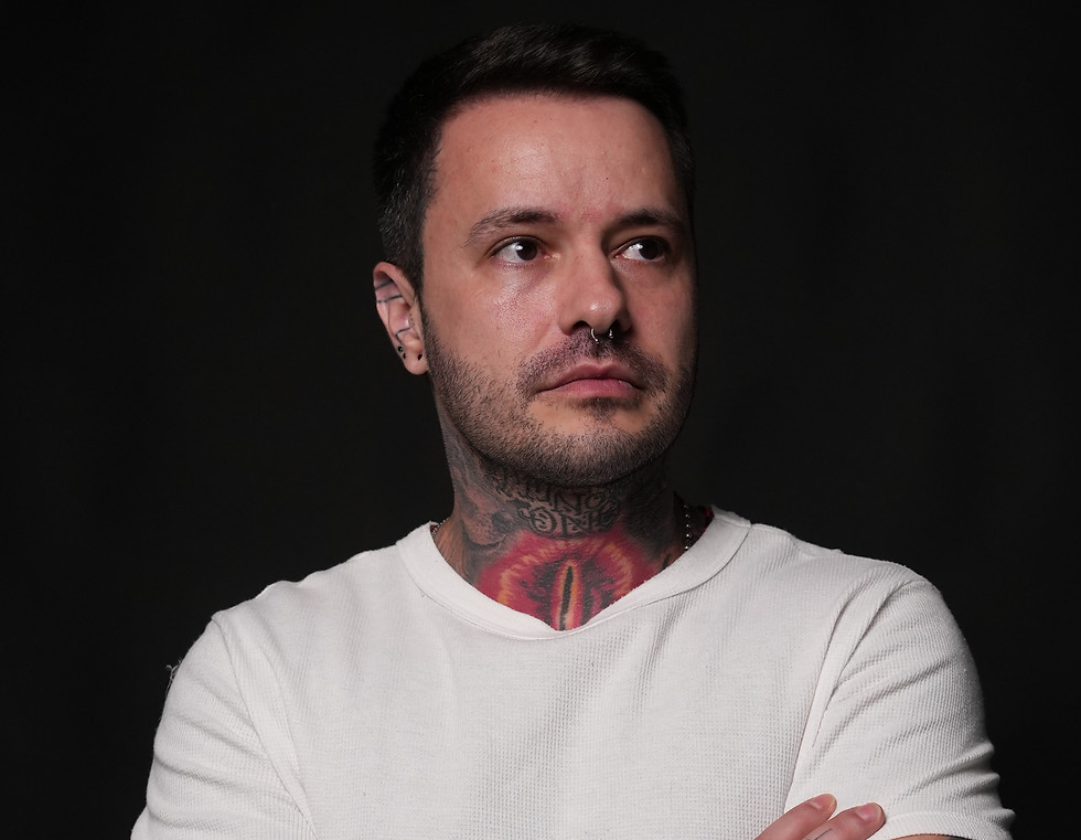 Tatuador com camiseta clara exibindo tatuagens nos braços cruzados, no Kreyner La Scala Tattoo Ateliê