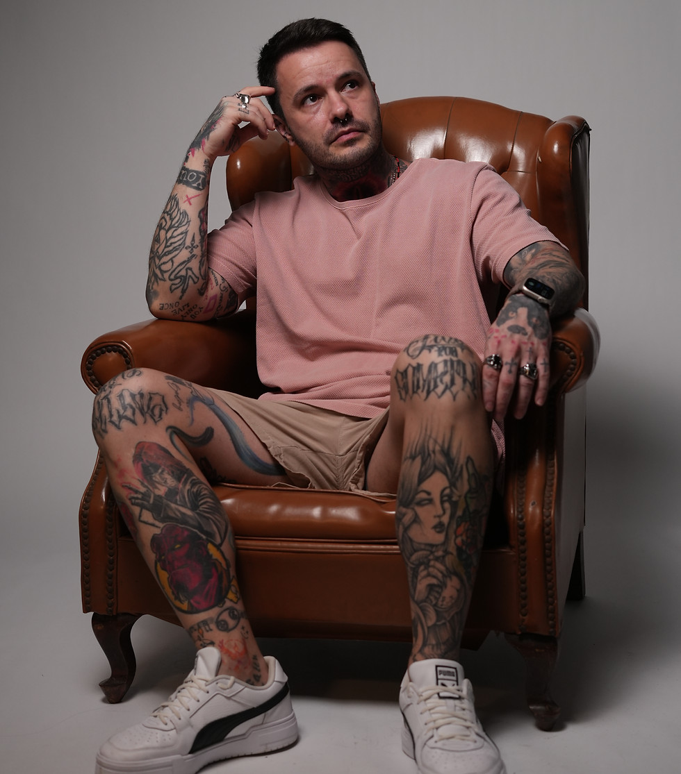 Artista tatuador sentado em poltrona, com corpo tatuado e expressão confiante no Kreyner La Scala Tattoo Ateliê