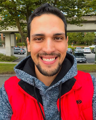 Foto do Leandro Alves de Sousa com um casaco vermelho e cinza, sentado e sorrindo olhando para a a câmera.