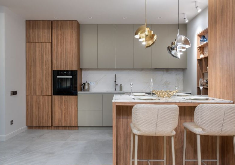 Modern kitchen with wooden cabinets, marble counter, and elegant lighting. Two stools at the island, and a tidy, minimalist design.