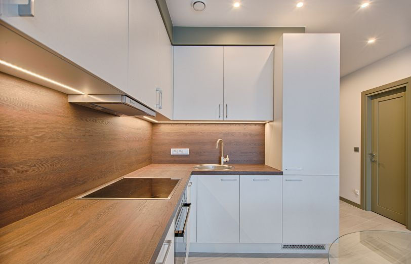 Modern kitchen with white cabinets, wood countertops, and stainless steel sink. Under-cabinet lighting creates a warm ambiance. Minimalist decor.