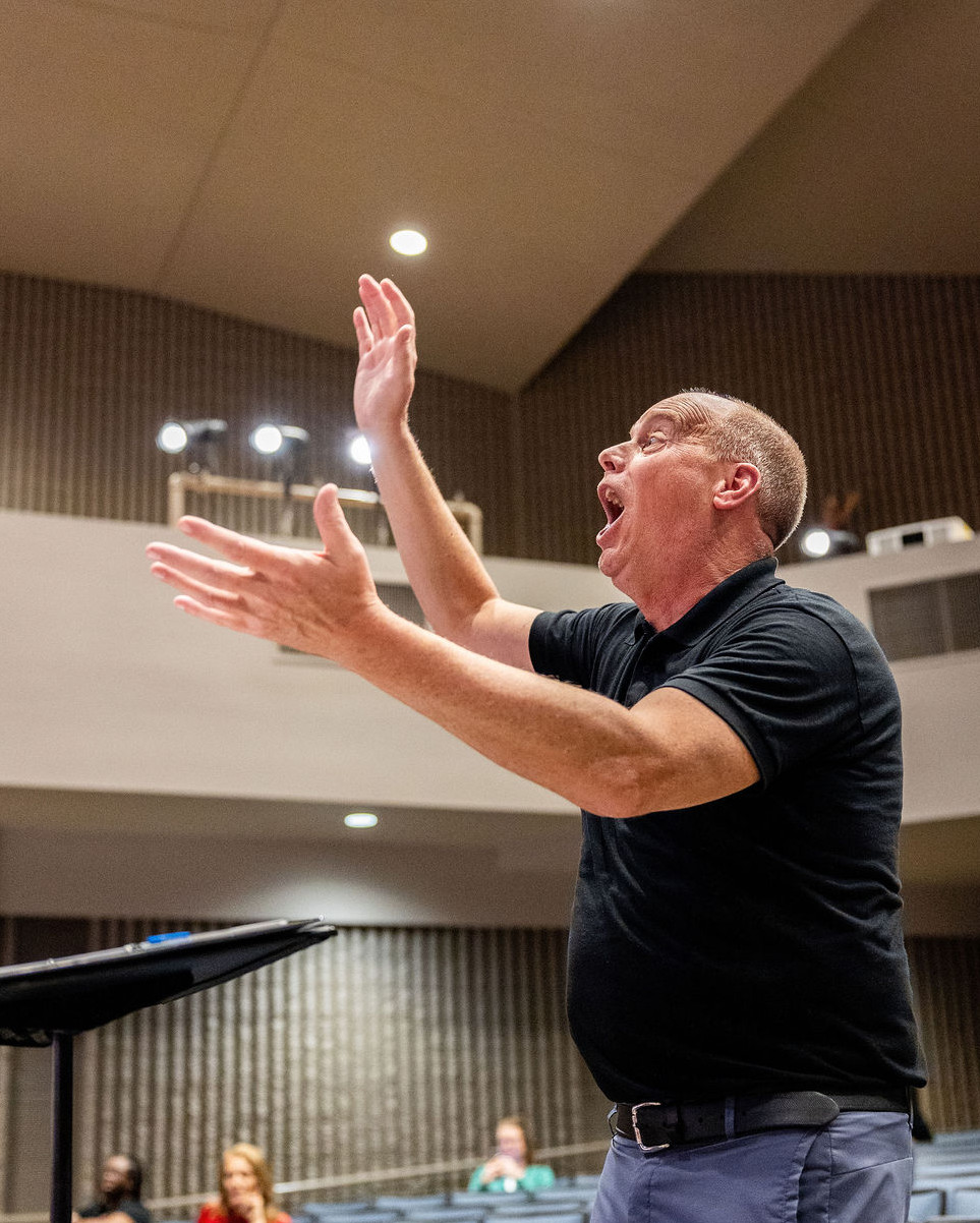 A man conducting we are your children in a theater.
