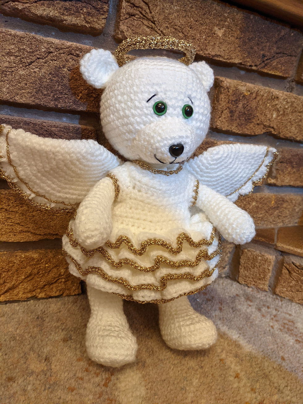A white bear dressed as an angel, with a gold edged white dress, wings and a gold halo