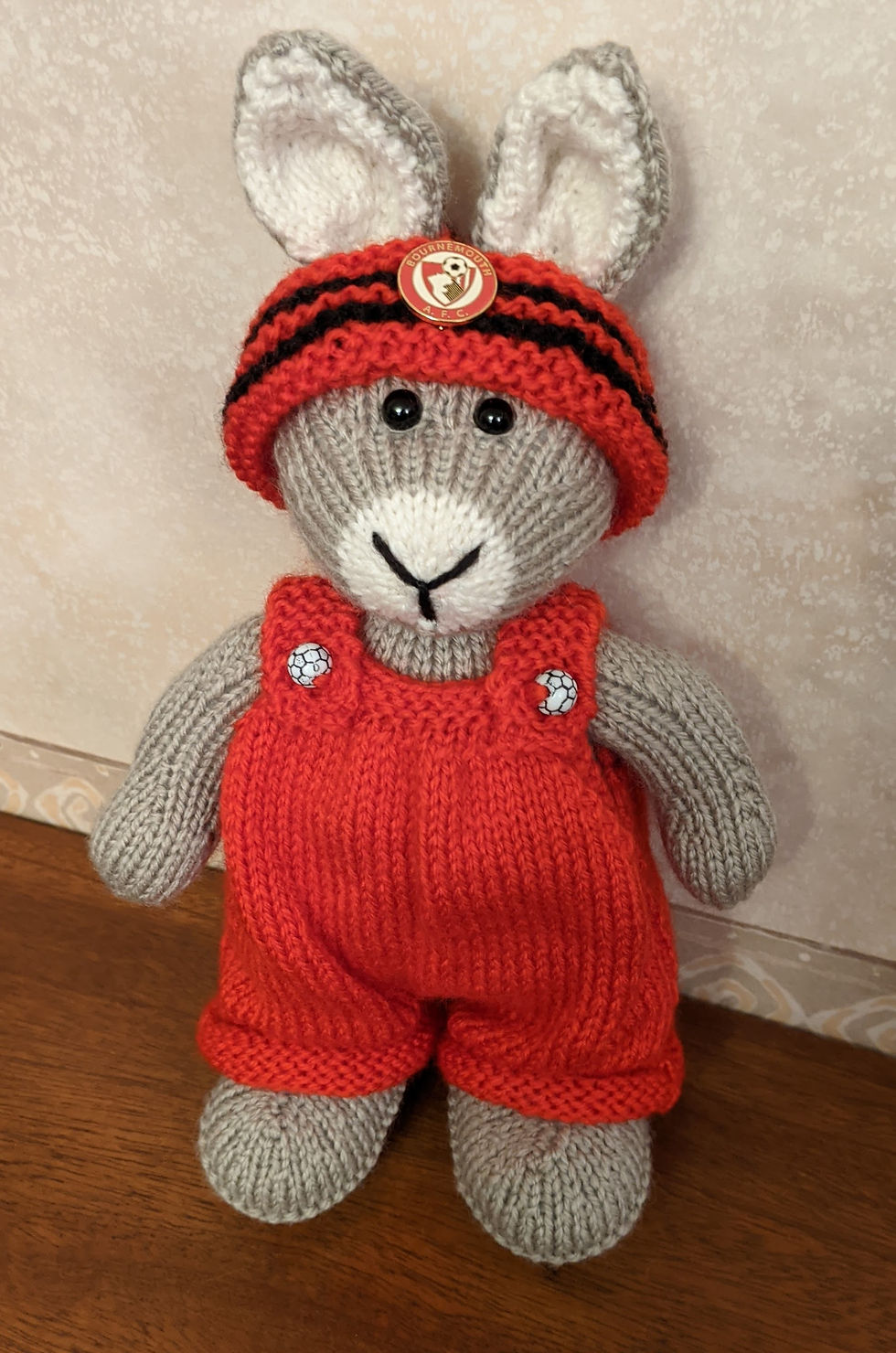 Toy rabbit wearing red dungarees and a red hat with black stripes. The hat has a Bournemouth football club badge on it.
