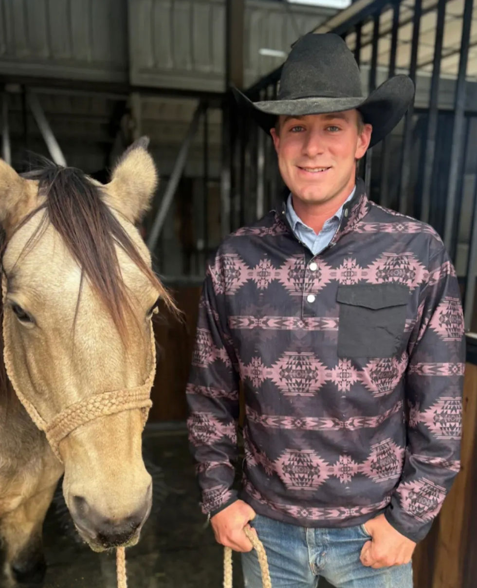 man wearing a hat and pullover standing next to a horse