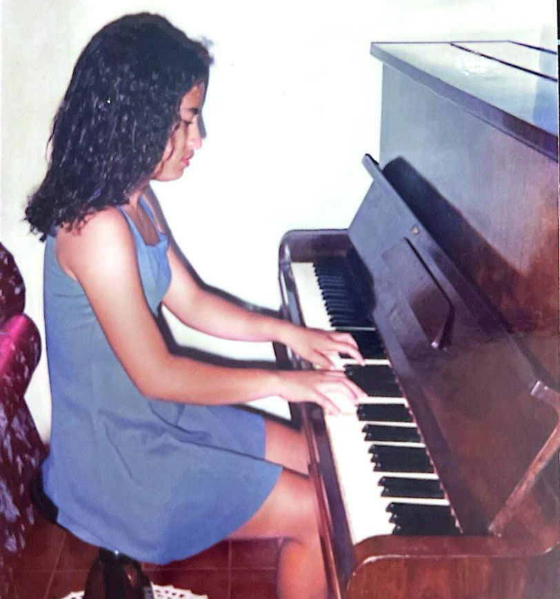 Luciana adolescente tocando piano, o primeiro instrumento que aprendeu na vida | Foto: Acervo Luciana Carrilo