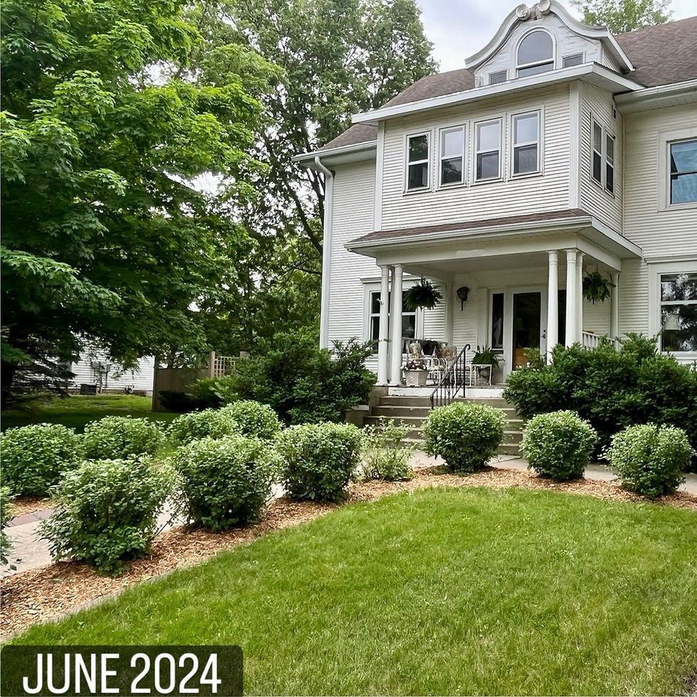 White house with porch, surrounded by greenery.