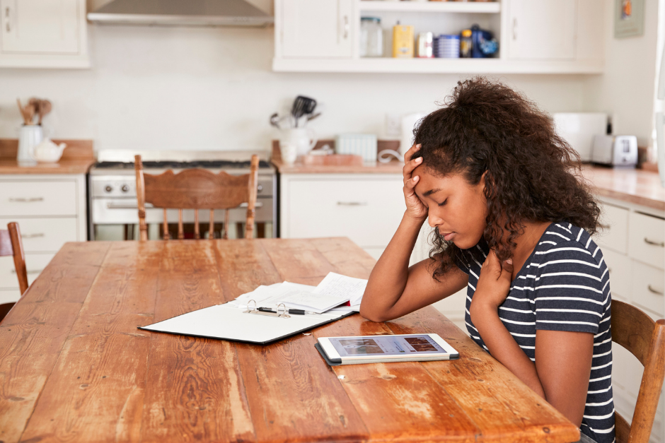 Teenage girl sitting at kitchen table very stressed while looking at tablet