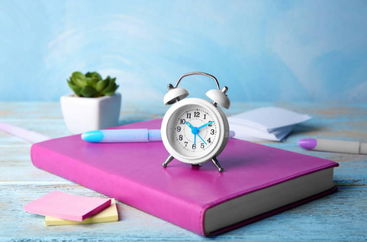 An analog alarm clock sitting atop a purple book.