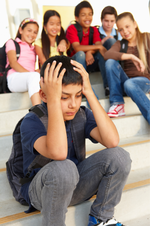 Young boy sitting on school steps while being laughed at from kids behind him