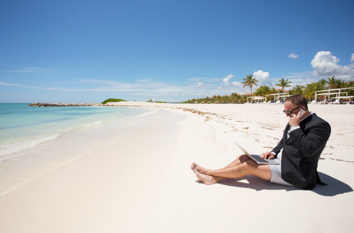 A man laying in the sand at the beach while on a work meeting call