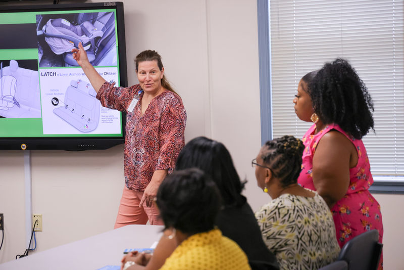 Woman pointing to a presentation about carseat safety while looking at the audience
