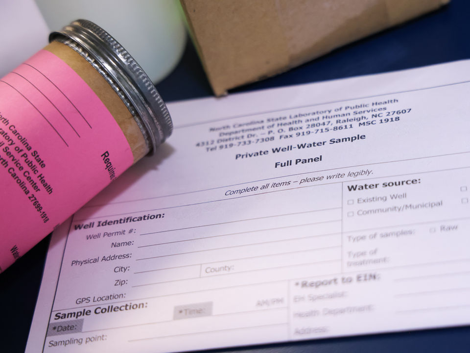 A water sample container sits on top of a well identification paper.