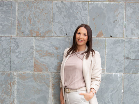 Vicky in light outfit standing against stone wall.