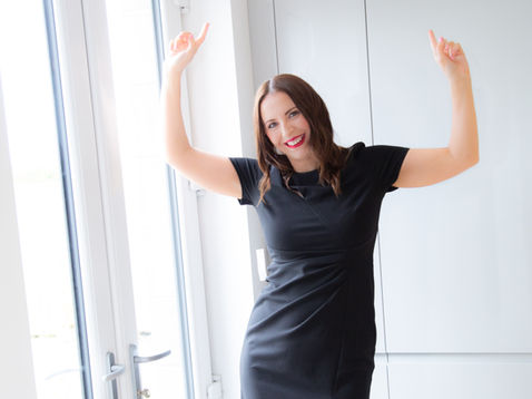 Vicky in black dress posing with arms raised.