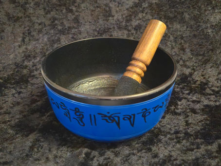 Blue singing bowl placed on a soft surface, reflecting natural light with a smooth, metallic finish. Used in sound healing and meditation practices for its calming tones.