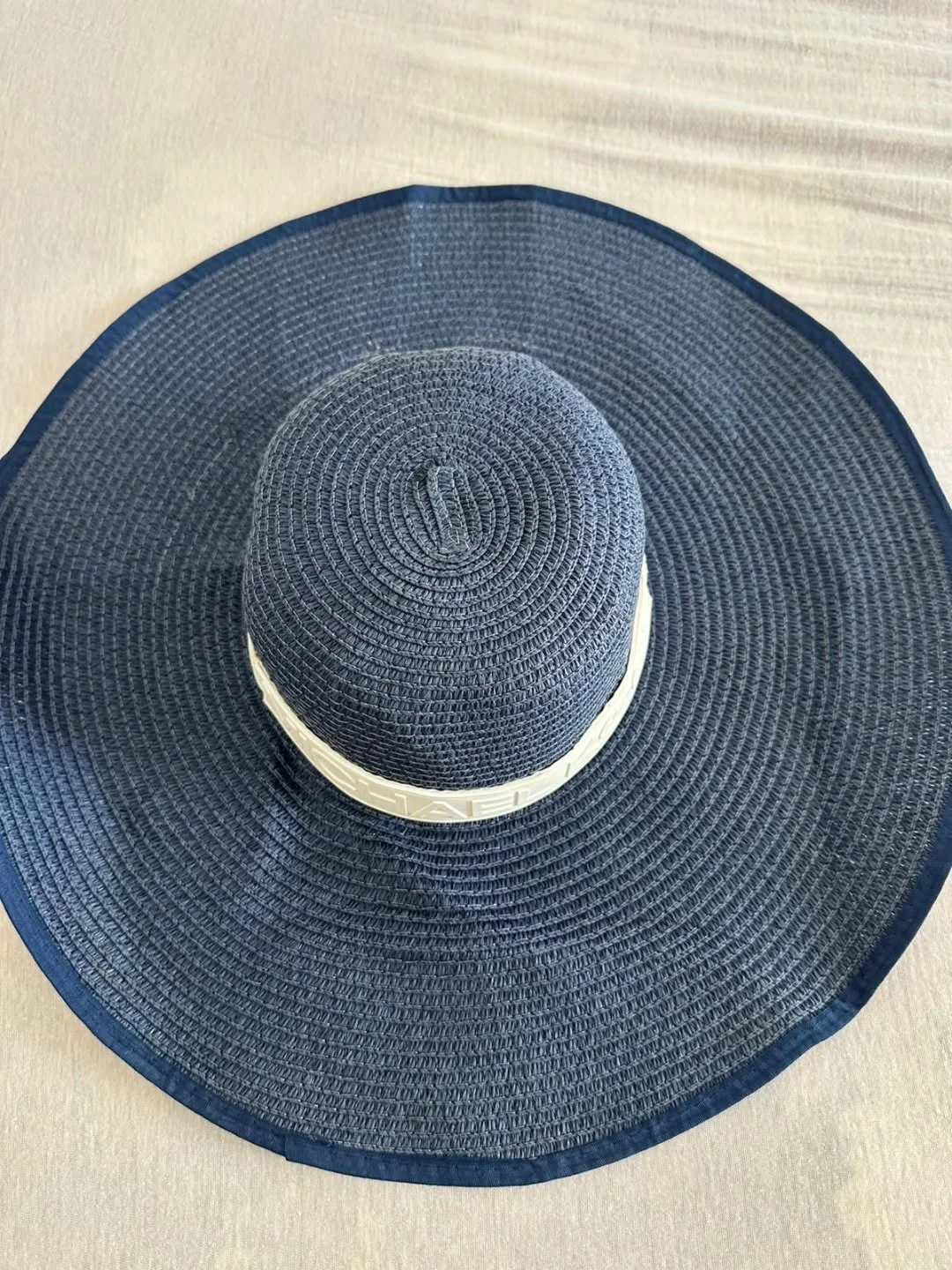 Top view of a navy blue wide-brim straw sun hat with a white band on a light surface.