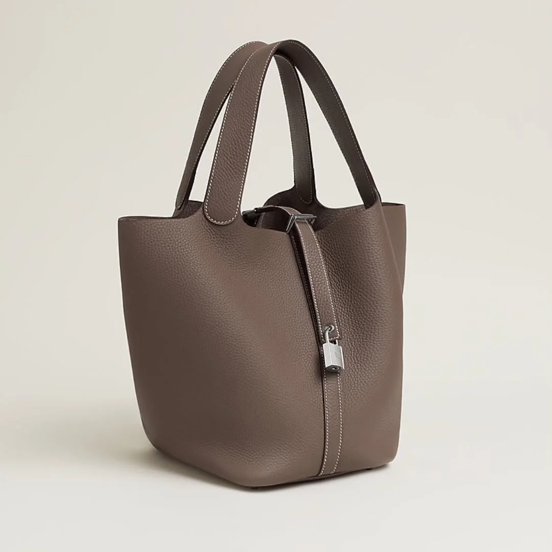 Taupe leather bucket tote bag with double handles and a silver padlock detail, photographed on a plain light background