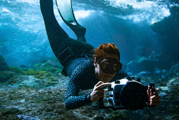 Underwater portrait portraying Belgian underwater photographer Ann Cools, holding underwater camera housing, wearing orca wetsuit