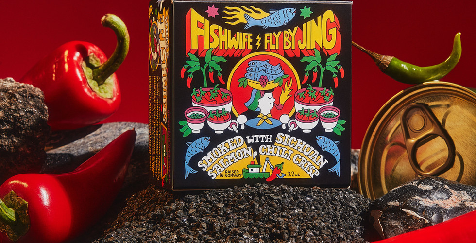 Stylized Fishwife x Fly by Jing product photography features a black box of tinned fish surrounded by chilis and tinned fish cans on a red background.