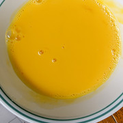 A white bowl holds the egg wash. It is a rich yellow and very liquid.