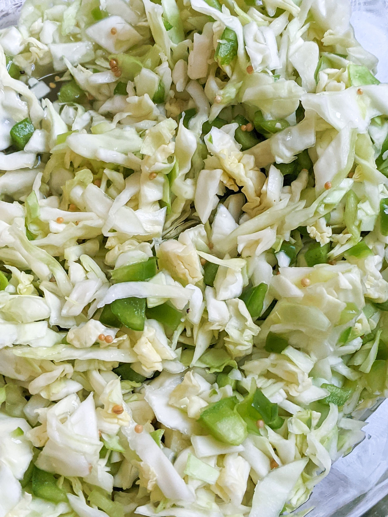 A close up of pepper hash. It's a mixture of shredded cabbage, green peppers, mustard seed. The salad is glistening slightly because it is coated in a vinegar mixture..