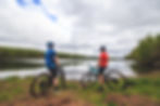 Cyclists pause to admire the tranquil lake views in Cuyuna Country, surrounded by lush greenery and expansive skies.