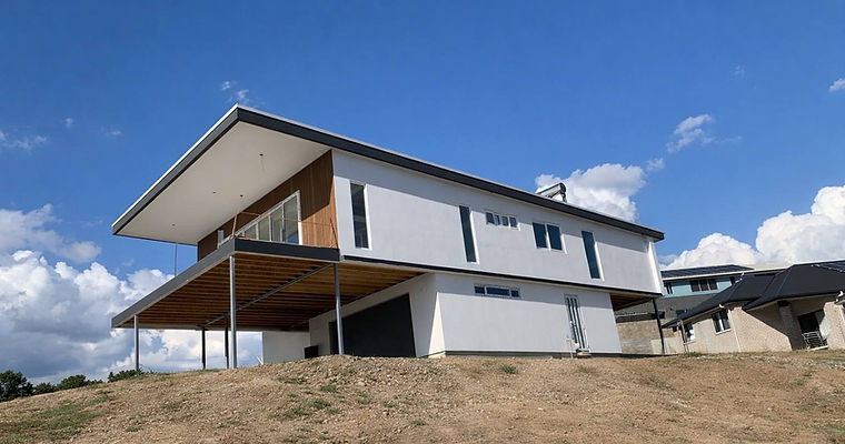 Modern architectural new build home on an elevated block, featuring a flawless, durable white acrylic render finish applied by JT Industries & Co to complement the timber cladding.