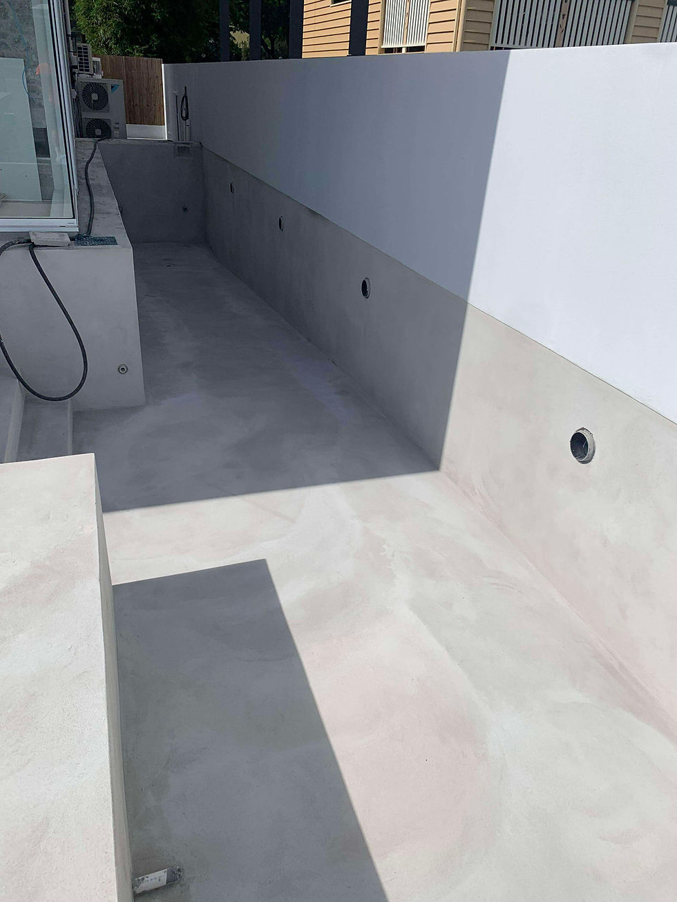 Empty concrete lap pool under construction, showcasing a freshly applied, perfectly smooth grey cement render on the interior walls and floor by the experts at JT Industries & Co.