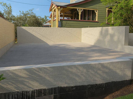 Detail of a durable, textured bagged cement render applied to a low block wall, enclosing a newly poured concrete pad to create a functional and stylish outdoor foundation.