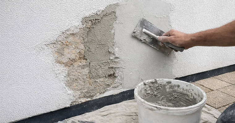 Close-up of an artisan using a trowel to apply fresh cement render to a damaged textured wall, showcasing expert render patching and seamless facade restoration techniques by JT Industries & Co.