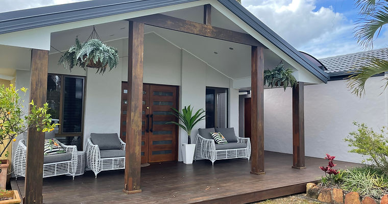 Front facade with a coat of white paint on the walls all greenscaping blending nicely with the timber deck and beams