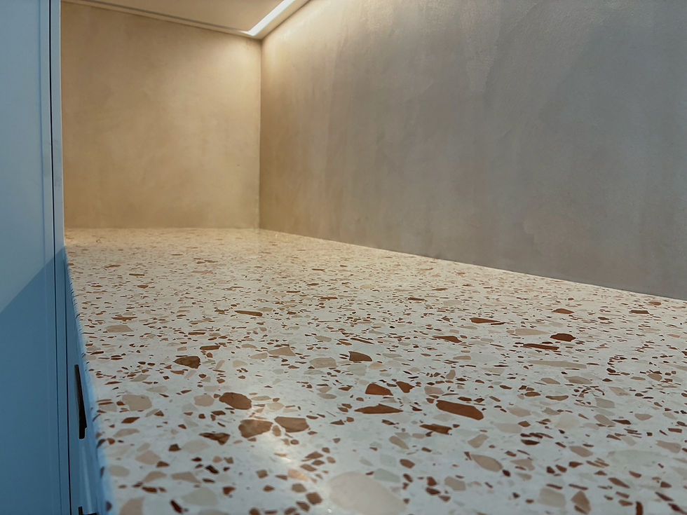 Smooth terrazzo countertop with beige and brown speckles, set against a Microcement splashback in Kitchen. Soft overhead lighting creates a calm mood.