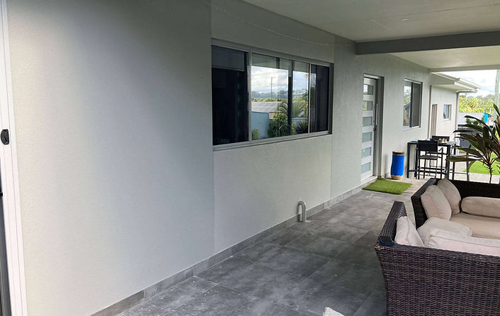 alfresco area of a home in Alex Heads showcasing a flawless grey cement render and durable exterior painting by JT Industries & Co, creating a seamless and modern outdoor living space.
