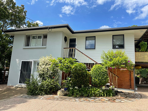 Grey coloured render mixing in nicely with the white cladding and black gutters gardern in the middle of walkway. Brisbane bright blue sky