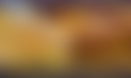 A hand holds a large gold ring amid many others on display. The scene is vibrant with shimmering gold jewelry against a red backdrop.