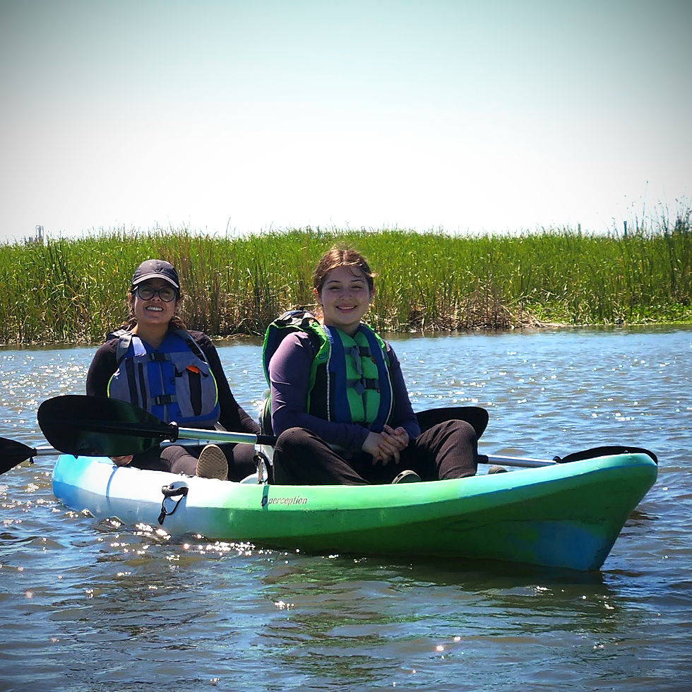 Two young people smiling while sitting in tandem kayak on water
