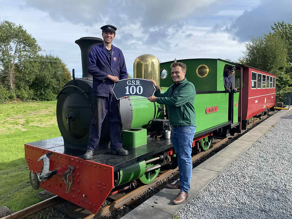 Two people posing with a.green steam train holding a 'GSR 100' headboard.