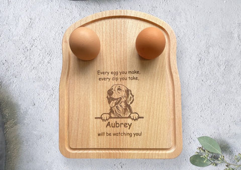 Sweet pea laser boutique wooden dippy egg board. The dippy egg board is the same shape as a slice of bread and shows a labrador dog peeking over an edge. the text reads 'every egg you make, every dip you take, aubrey will be watching you.' the dog name and breed can be customised
