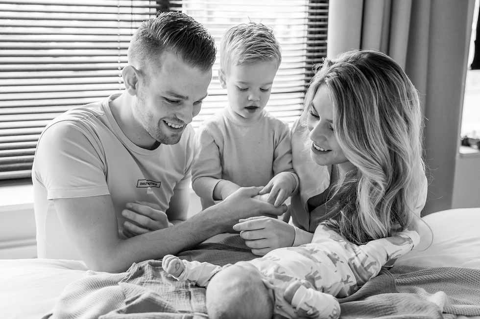 Newborn foto shoot. Ouders zitten op bed en kijken trots naar de baby. Lifestyle fotoshoot