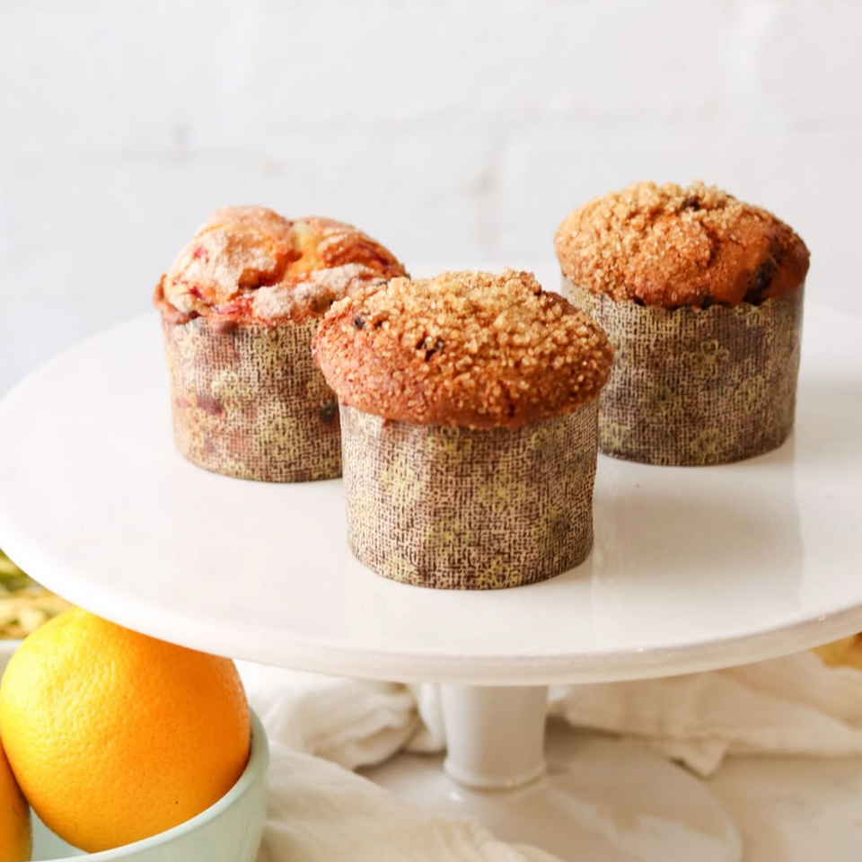 Muffins on a cake serving platter with oranges and a towel in the background